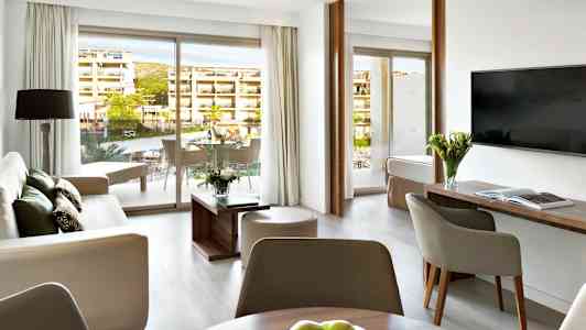 Modernisti sisustettu hotellisviitti, jossa oleskelualue, pöytä ja parveke. (Tekoälyn luoma teksti)