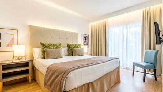 Hotellihuone, jossa on parivuode, sivupöytä, tuoli ja iso ikkuna. (Tekoälyn luoma teksti)