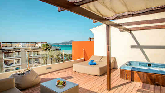 Parveke, jossa poreamme, aurinkotuoli ja istuimia, näkymä merelle ja rakennuksiin. (Tekoälyn luoma teksti)