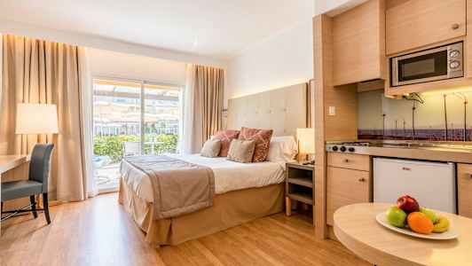 Hotellihuone, jossa on suuri sänky, kirjoituspöytä ja keittiö sekä parveke näköalalla. (Tekoälyn luoma teksti)