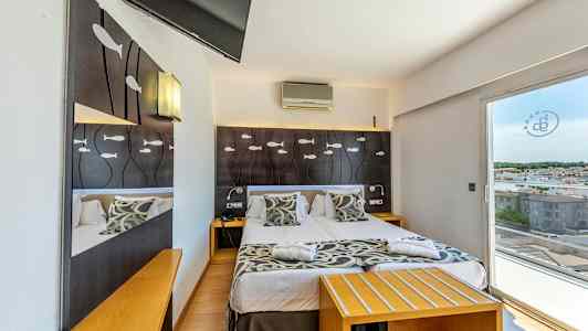 Hotellihuone, jossa on parivuode, koristeena kalakuvioita sängyn päädyssä ja näkymä kaupunkiin lasiovien kautta. (Tekoälyn luoma teksti)