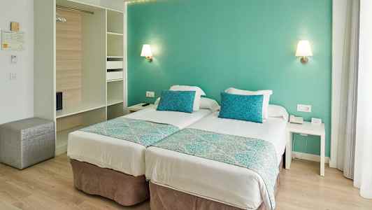 Hotellihuone, jossa on kaksi erillistä vuodetta, turkoosit tyynyt ja seinät. (Tekoälyn luoma teksti)