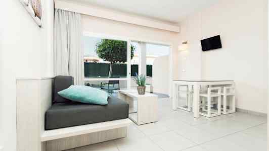 Nykyaikainen valoisa huone, jossa on istuimia, pöytä ja kasvi, suuret ikkunat ja näkymä puutarhaan. (Tekoälyn luoma teksti)