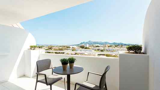 Parveke, jossa pöytä ja tuolit, näkymä ympäröiviin rakennuksiin ja vuorille. (Tekoälyn luoma teksti)