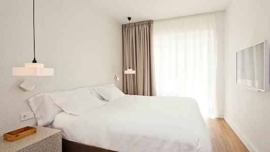 Huone, jossa on sänky, valkoisia lakanoita ja verhot sekä seinään kiinnitetty televisio. (Tekoälyn luoma teksti)