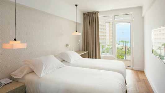 Hotellihuone, jossa kaksi yhden hengen vuodetta, vaalea sisustus ja parveke merinäköalalla. (Tekoälyn luoma teksti)