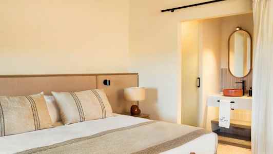 Hotellihuone, jossa on sänky, lamppu ja näkyvä osa kylpyhuonetta. (Tekoälyn luoma teksti)