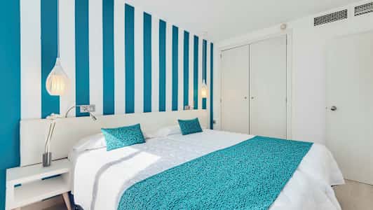 Makuuhuone, jossa sänky, sinivalkoraidallinen seinä ja valkoiset huonekalut. (Tekoälyn luoma teksti)