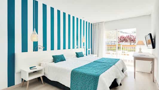 Moderni hotellihuone, jossa raidallinen seinä, valkoiset ja turkoosit vuodevaatteet sekä parveke näkymineen. (Tekoälyn luoma teksti)