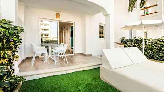 Ulkoterassi, jossa pöytä ja tuolit sekä aurinkotuolit ja varjo nurmikolla. (Tekoälyn luoma teksti)