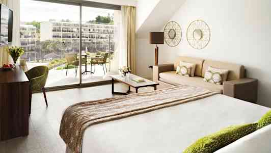 Valoisa hotellihuone, jossa on sänky, sohva ja parveke ulkona. (Tekoälyn luoma teksti)