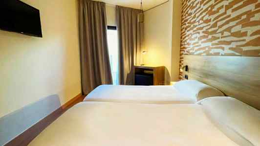 Kaksi yhden hengen sänkyä hotellihuoneessa, jossa on kuvioitu pääty ja televisio seinällä. (Tekoälyn luoma teksti)