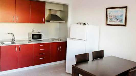 Keittiö, jossa on punaiset kaapit, jääkaappi ja ruokailutila pöydällä ja tuoleilla. (Tekoälyn luoma teksti)