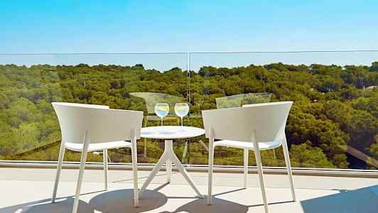 Kaksi valkoista tuolia pyöreän pöydän ääressä, kaksi lasia parvekkeella, näkymä metsään. (Tekoälyn luoma teksti)