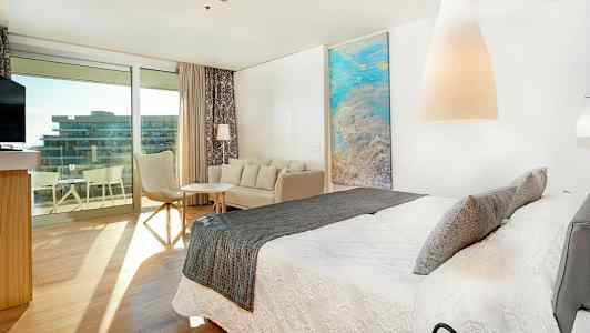 Moderni hotellihuone, jossa iso sänky, istuma-alue ja parvekkeelle käynti. (Tekoälyn luoma teksti)