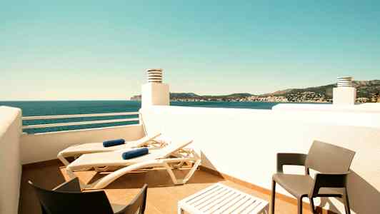 Terassi, jolla on aurinkotuoleja, pöytä ja kaksi tuolia sekä näkymä merelle ja ympäröivään maisemaan. (Tekoälyn luoma teksti)