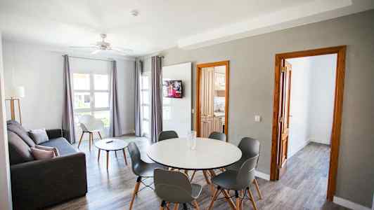 Olohuone, jossa harmaa sohva, ruokapöytä tuoleilla ja televisio seinällä. (Tekoälyn luoma teksti)