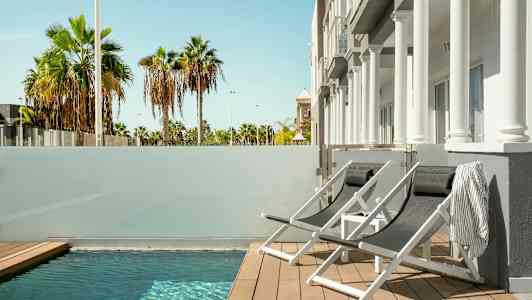 Aurinkotuoleja pienen uima-altaan äärellä, näkymä palmuihin. (Tekoälyn luoma teksti)