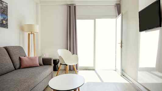 Valoisa ja moderneisti sisustettu olohuone, jossa harmaa sohva, valkoinen tuoli ja pyöreä sohvapöytä. (Tekoälyn luoma teksti)