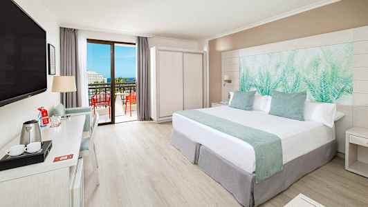 Moderni hotellihuone, jossa parivuode, kirjoituspöytä, TV ja parveke näkymällä. (Tekoälyn luoma teksti)