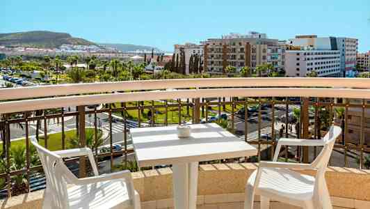 Näkymä parvekkeelta, jossa pöytä ja kaksi tuolia, kaupungin ja vihreiden alueiden yli. (Tekoälyn luoma teksti)