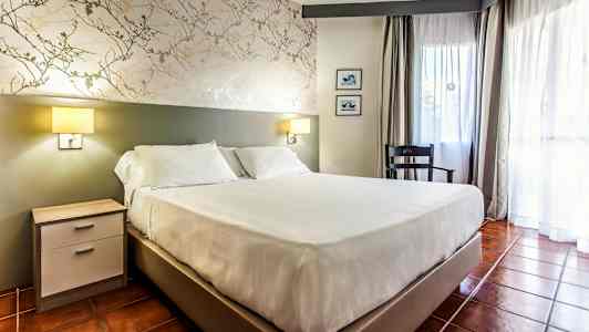 Huone, jossa on parivuode, yöpöytä, tuoli ja ikkunat verhoilla. (Tekoälyn luoma teksti)