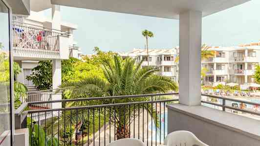 Näkymä parvekkeelta useisiin valkoiseksi maalattuihin rakennuksiin, joissa on vehreitä palmuja ja uima-allasalue alhaalla. (Tekoälyn luoma teksti)