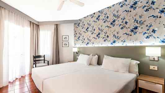 Hotellihuone, jossa on kaksi yhden hengen vuodetta ja kuvioitu seinäkoriste. (Tekoälyn luoma teksti)