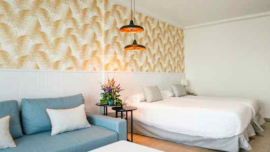 Hotellihuone, jossa sininen sohva, parivuode ja koristeellinen tapetti. (Tekoälyn luoma teksti)