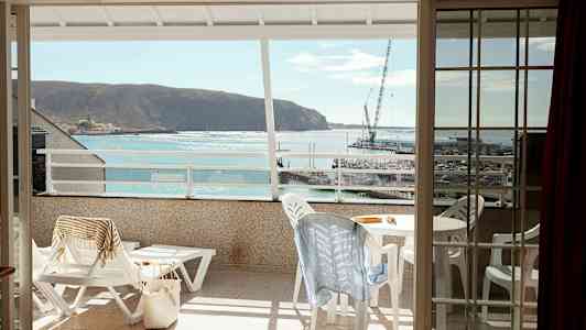 Näköala parvekkeelta merelle ja pieneen satamaan, parvekkeella ulkokalusteet ja aurinkotuolit. (Tekoälyn luoma teksti)