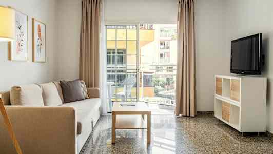 Olohuone, jossa on sohva, sohvapöytä ja televisio sekä suuret ikkunat parvekkeelle. (Tekoälyn luoma teksti)