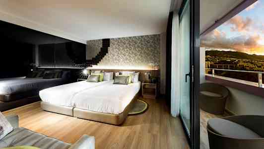 Moderni hotellihuone, jossa on kaksi sänkyä, peiliseinä ja parveke näkymällä maisemaan. (Tekoälyn luoma teksti)