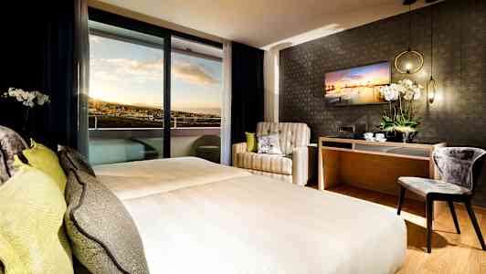 Hotellihuone, jossa on parivuode, nojatuoli, työpöytä ja näkymä auringonlaskuun. (Tekoälyn luoma teksti)