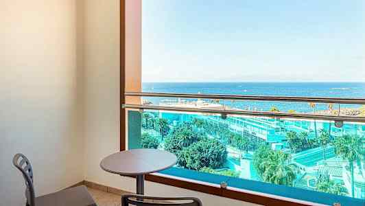 Parveke, jossa on pöytä ja tuolit, näkymä merelle ja hotelliin. (Tekoälyn luoma teksti)