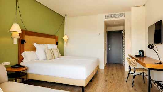 Hotellihuone, jossa on leveä sänky, työpöytä ja vihreä seinä. (Tekoälyn luoma teksti)