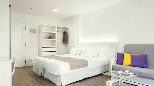 Valoisa hotellihuone, jossa on parivuode, sohva ja vaatekaappi. (Tekoälyn luoma teksti)