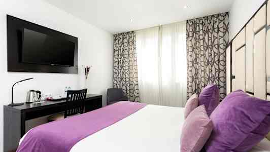 Hotellihuone, jossa on parivuode, violetit vuodevaatteet ja tyynyt, työpöytä tuoleineen ja seinälle asennettu televisio. (Tekoälyn luoma teksti)