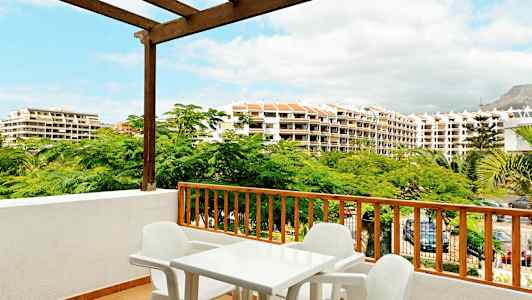 Näkymä parvekkeelta muovisten pöytien ja tuolien kanssa, ympärillä vihreitä puita ja rakennuksia taustalla. (Tekoälyn luoma teksti)