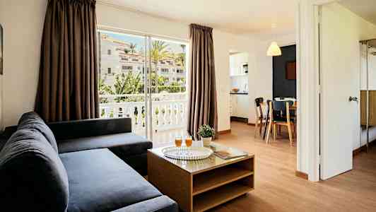 Olohuone, jossa tumma sohva, sohvapöytä ja näkymä parvekkeelle sekä vehreään ympäristöön. (Tekoälyn luoma teksti)