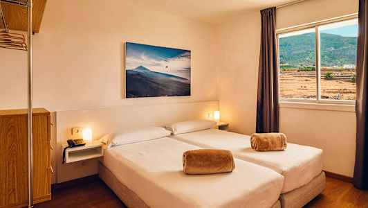 Hotellihuone, jossa on kaksi erillissänkyä, ikkuna näkymällä maisemaan ja seinällä oleva maalaus. (Tekoälyn luoma teksti)