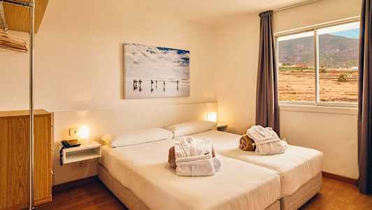 Vaalea hotellihuone, jossa on parivuode, ikkuna näkymällä maisemaan ja seinämaalaus sängyn yläpuolella. (Tekoälyn luoma teksti)