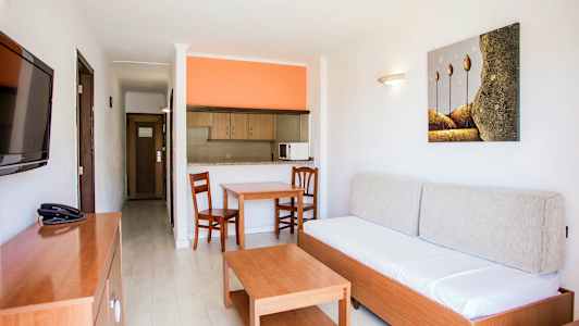 Asunnon sisustus, jossa sohva, pöytä, kaksi tuolia ja avoin keittiö oranssilla seinällä. (Tekoälyn luoma teksti)