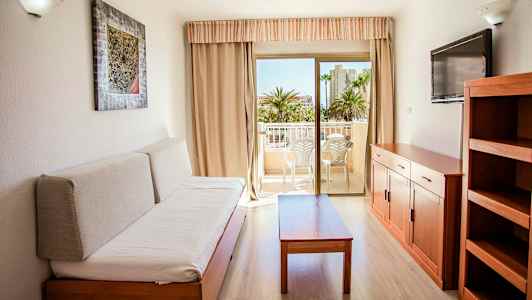 Sisustettu huone, jossa sohva, pöytä, televisio ja hylly. Pääsy parvekkeelle, jossa istumapaikat. (Tekoälyn luoma teksti)