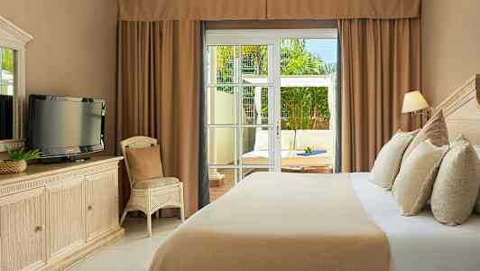 Hotellihuone, jossa on sänky, televisio lipaston päällä ja tuoli. Lasiovet johtavat ulkoterassille, jossa on istuimia. (Tekoälyn luoma teksti)