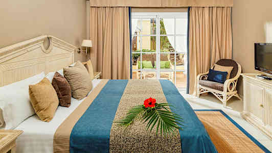 Kuva hotellihuoneesta, jossa on sänky, televisio ja näkymä terassille. (Tekoälyn luoma teksti)