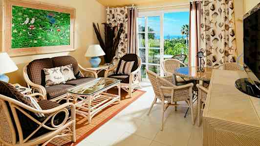 Olohuone, jossa on rottinkikalusteita, lasipöytä ja värikäs taulu seinällä. (Tekoälyn luoma teksti)