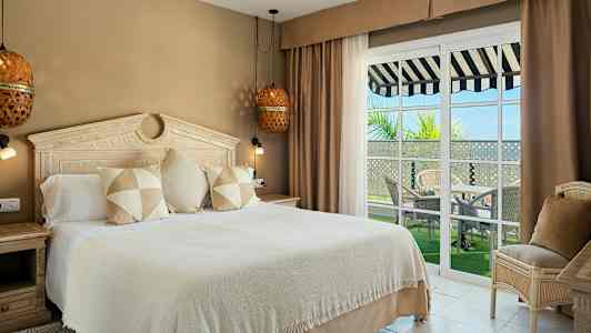 Hotellihuone, jossa on suuri sänky, tyylikäs sisustus ja ikkunat parvekkeelle, jolta on näkymä. (Tekoälyn luoma teksti)