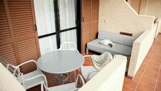 Tilava terassi, jossa valkoisia tuoleja pyöreän pöydän ympärillä ja harmaa sohva. (Tekoälyn luoma teksti)