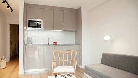 Moderni huone, jossa harmaa keittiö, rottinkituoli ja harmaa sohva. (Tekoälyn luoma teksti)