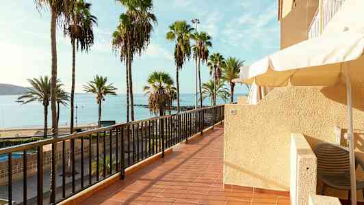 Terassi, jolta avautuu näkymä rannalle, jossa on palmuja ja merta. (Tekoälyn luoma teksti)